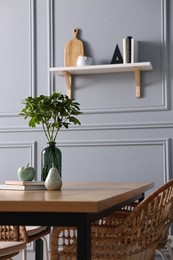 Photo of Vase with green branches, books and decor on wooden table in stylish dining room