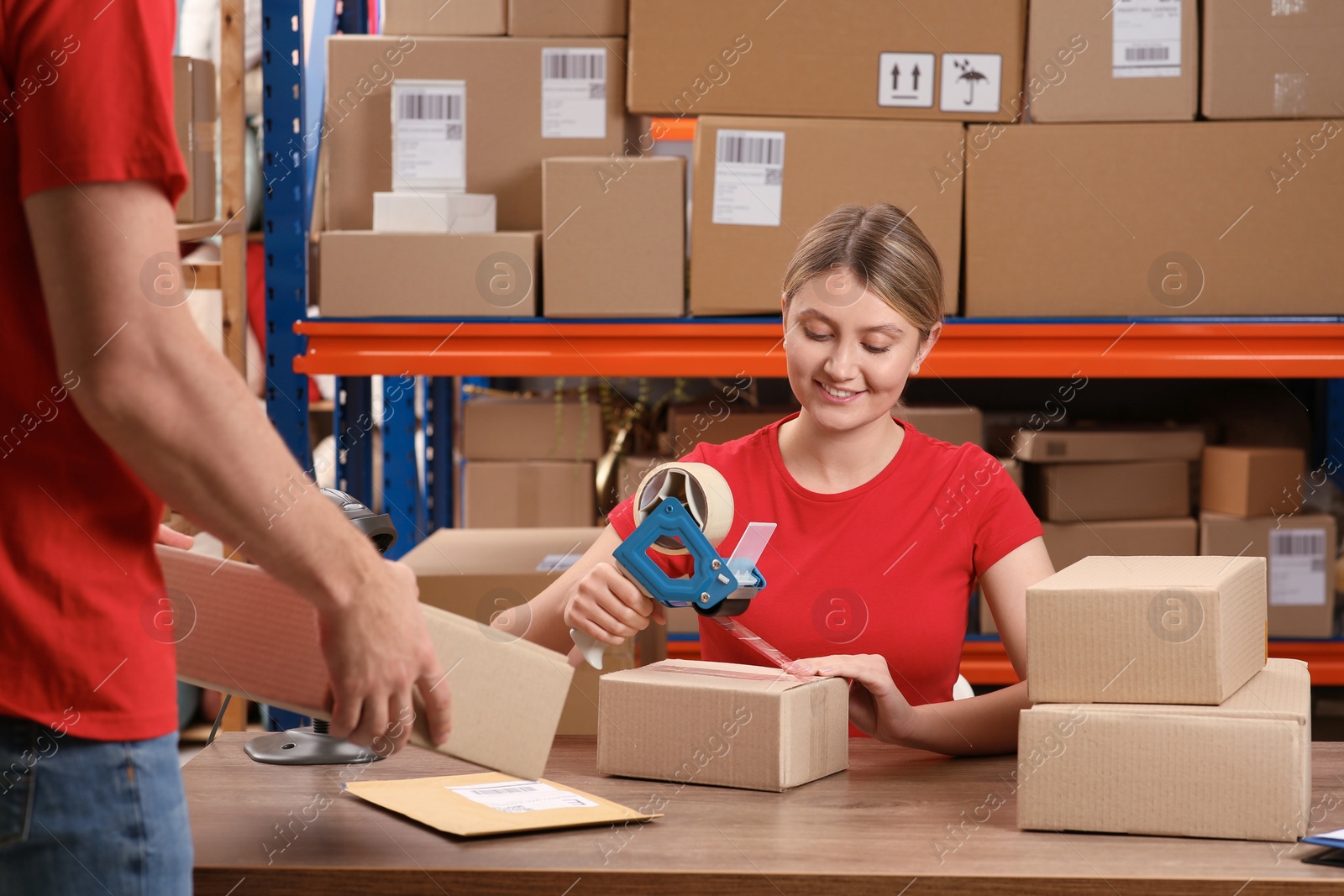 Photo of Man with cardboard boxes and woman packing parcel at post office