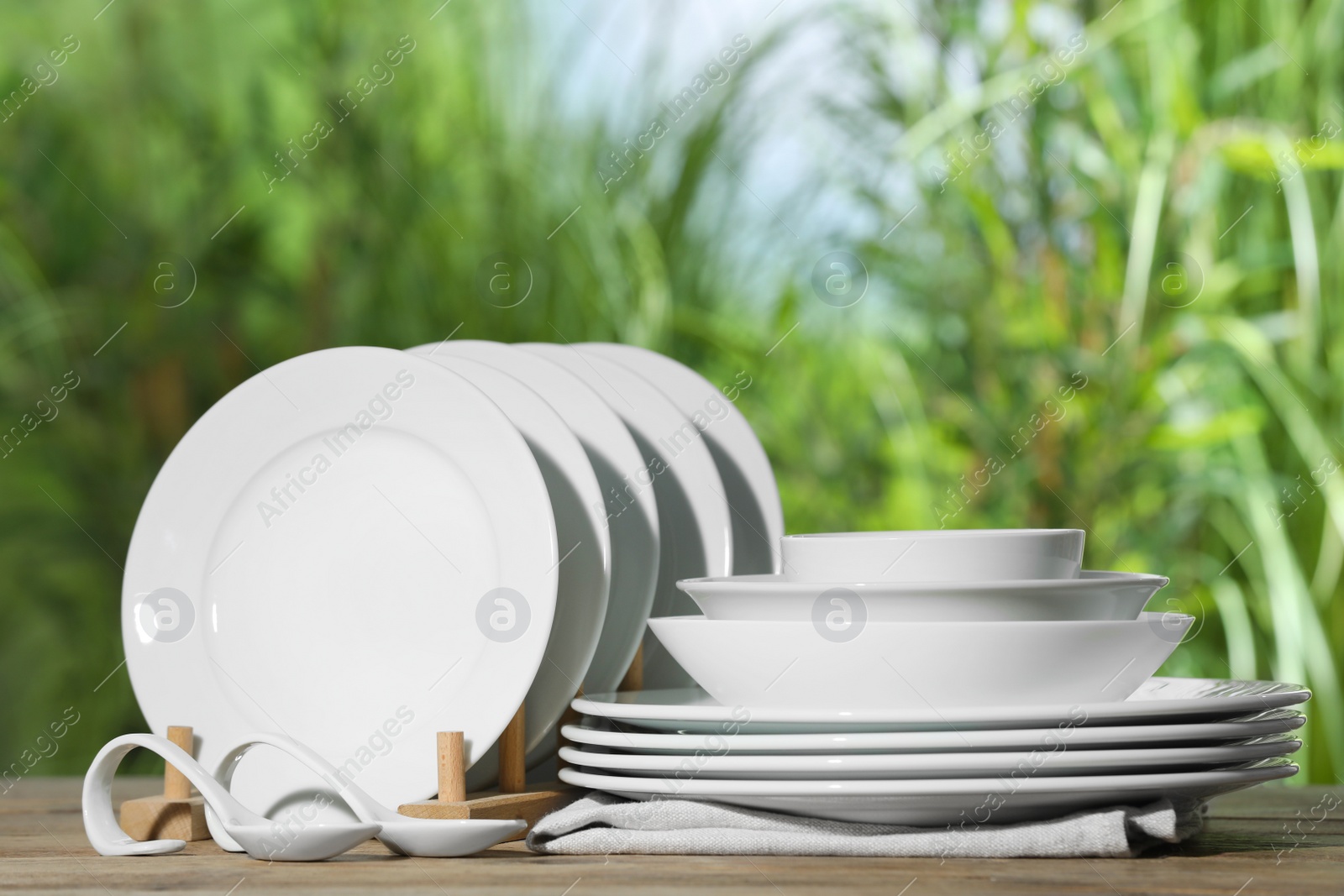 Photo of Set of clean dishware on wooden table against blurred background