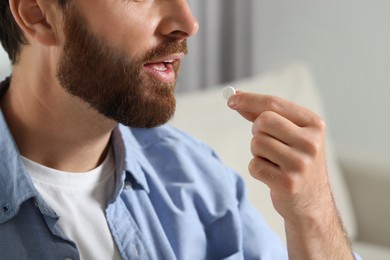 Bearded man taking pill indoors, closeup view