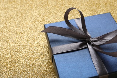 Photo of Blue gift box on golden background, closeup. Space for text