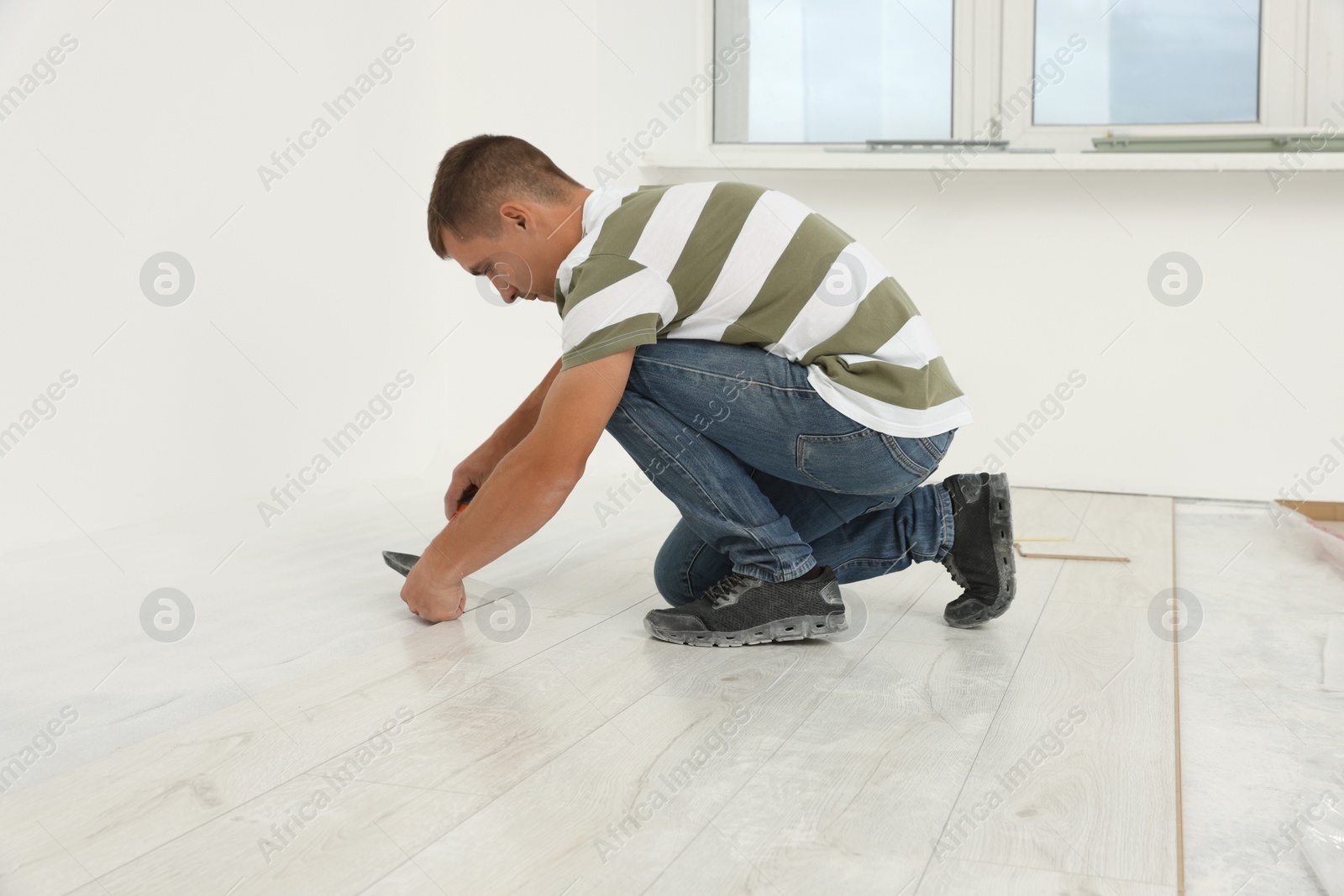 Photo of Professional worker using hammer during installation of new laminate flooring indoors