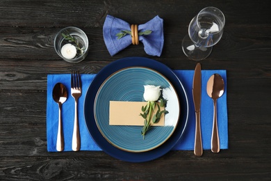 Elegant festive table setting with blank card on black wooden background, flat lay