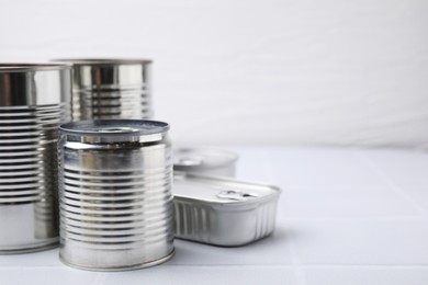 Photo of Many closed tin cans on white tiled table, closeup. Space for text