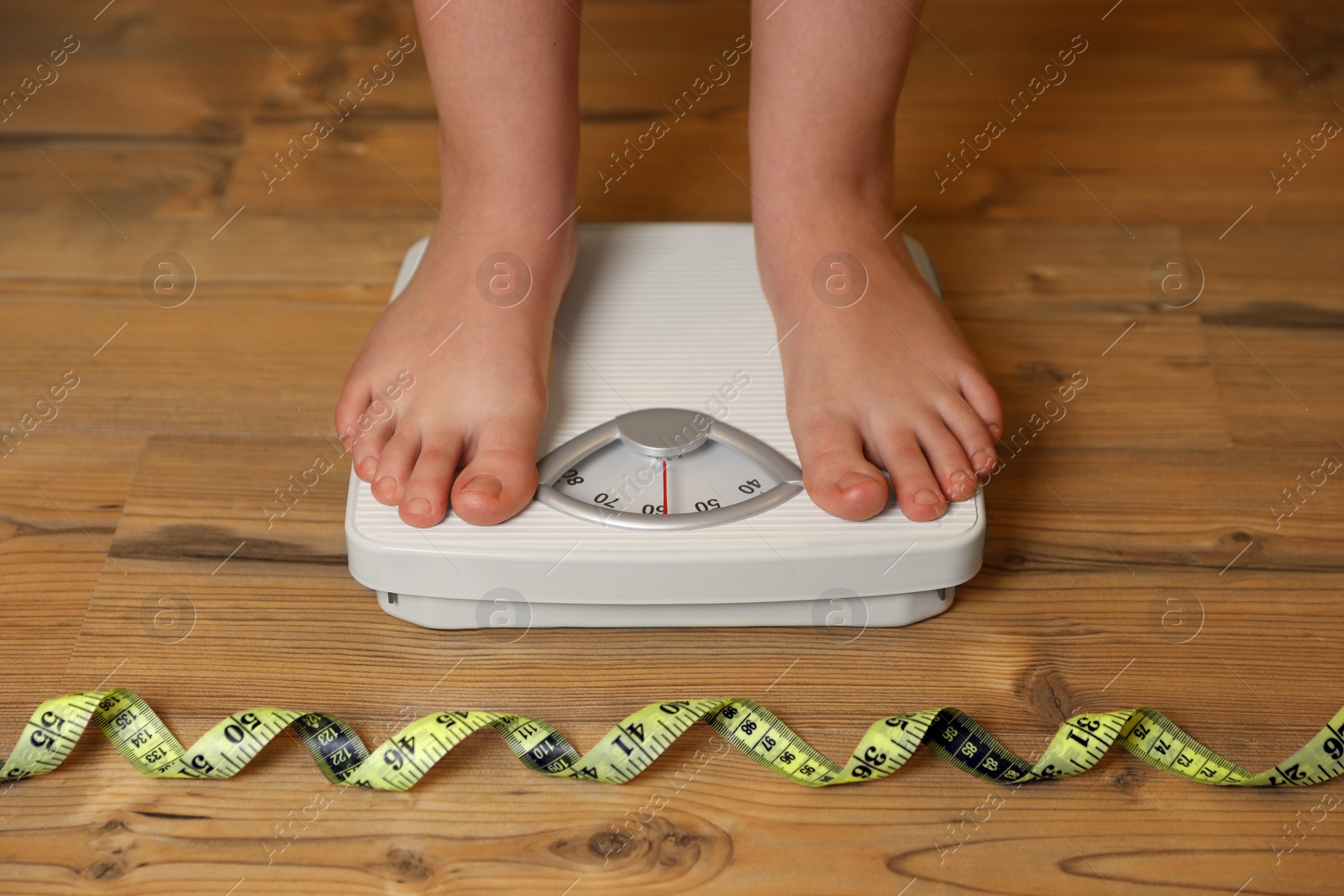 Photo of Overweight girl using scales near measuring tape on wooden floor, closeup