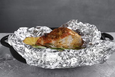 Photo of Tasty pork baked in foil and lemon on grey textured table