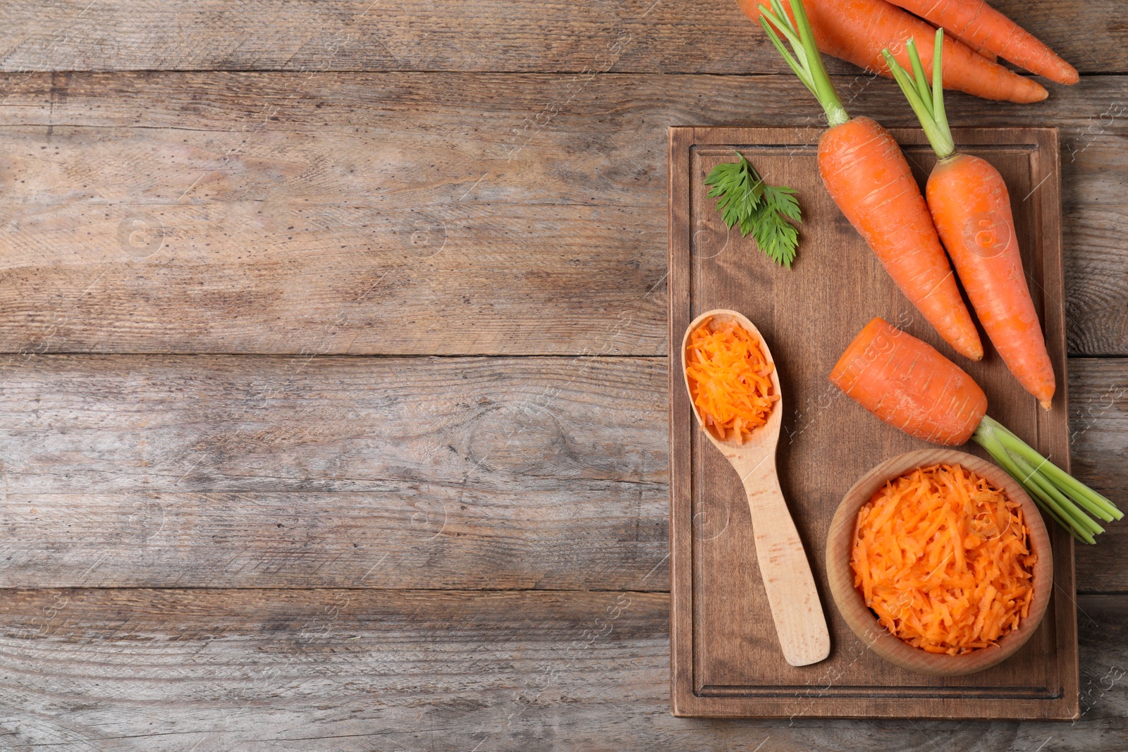 Photo of Board with fresh and grated carrots on wooden table, flat lay. Space for text