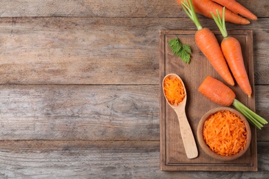 Photo of Board with fresh and grated carrots on wooden table, flat lay. Space for text