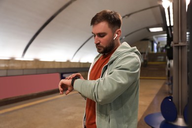 Photo of Young man with earphones waiting for train at subway station. Public transport
