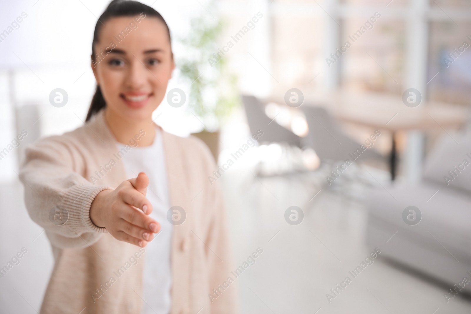 Photo of Happy young woman offering handshake indoors, focus on hand. Space for text