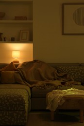 Stylish room interior with couch and lamp at night