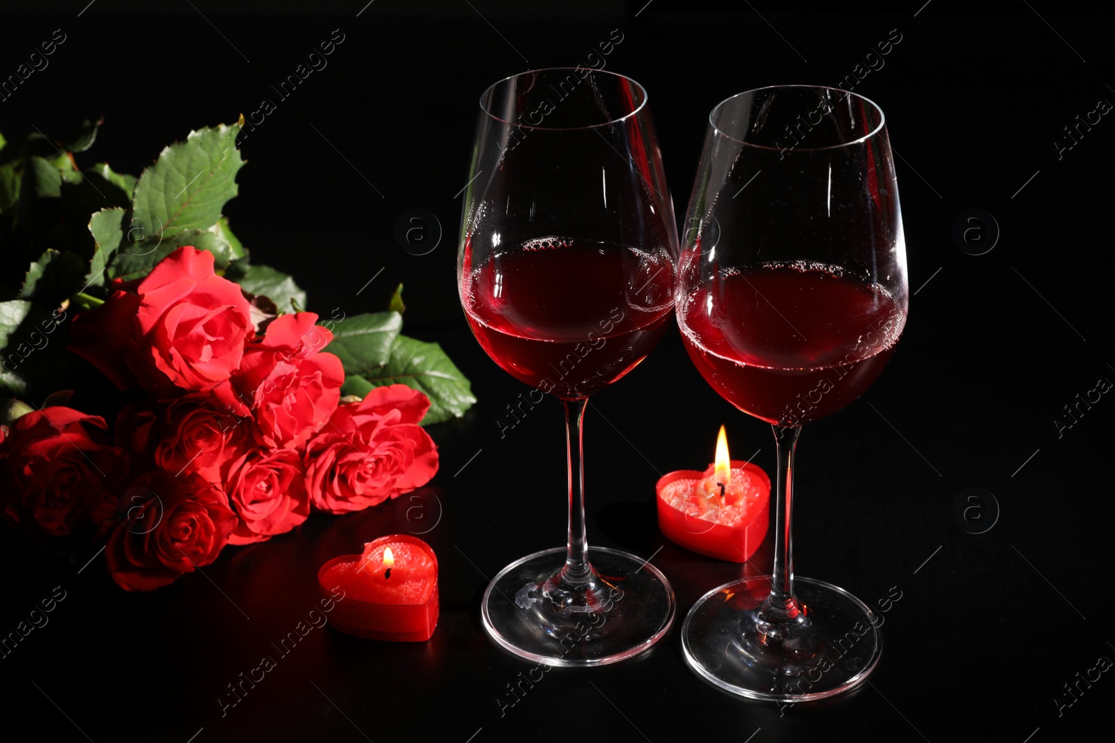 Photo of Glasses of wine, roses and heart shaped candles for romantic dinner on black table