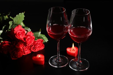 Glasses of wine, roses and heart shaped candles for romantic dinner on black table