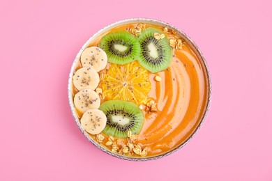 Photo of Bowl of delicious fruit smoothie with fresh banana, kiwi slices and granola on pink background, top view