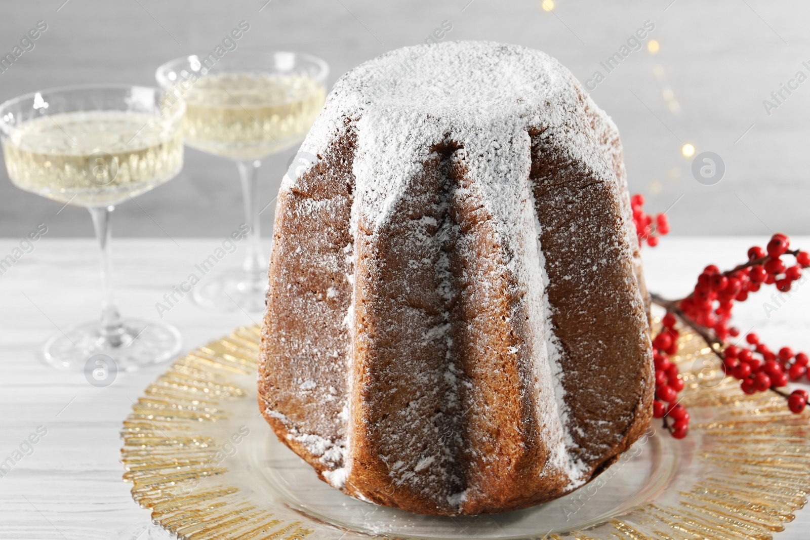 Photo of Delicious Pandoro cake decorated with powdered sugar and sparkling wine on white wooden table, closeup. Traditional Italian pastry