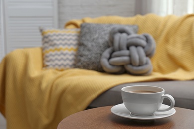 Cup of hot drink on table near sofa with pillows in living room