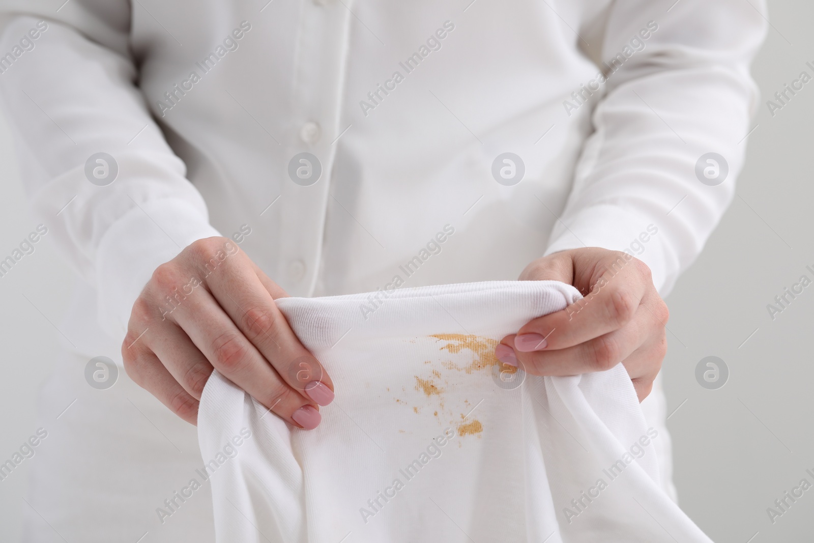 Photo of Woman holding shirt with stain against light background, closeup