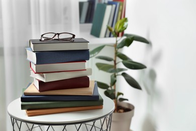 Stack of many different books and glasses on coffee table indoors. Space for text