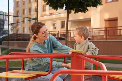 Happy nanny and cute little boy on carousel outdoors