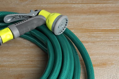 Photo of Green rubber watering hose with nozzle on wooden surface, closeup