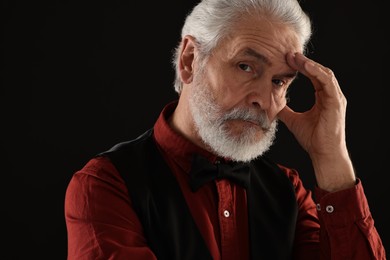 Senior man touching mustache on black background