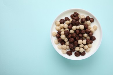 Photo of Breakfast cereal. Tasty corn balls with milk in bowl on light blue background, top view. Space for text