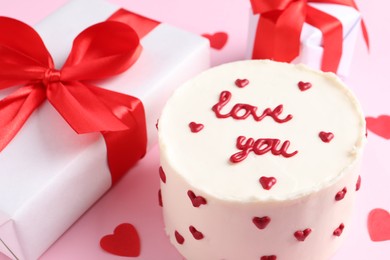 Photo of Bento cake with text Love You, gift boxes and paper hearts on pink table. St. Valentine's day surprise