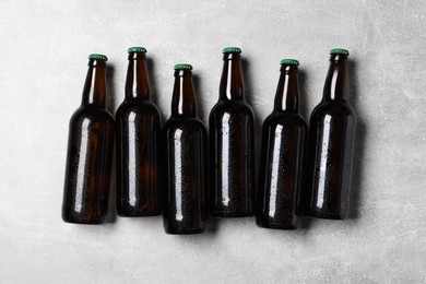 Glass bottles of beer on light grey background, flat lay