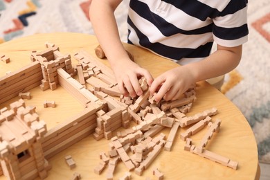 Photo of Little boy playing with wooden construction set at table indoors, closeup. Child's toy