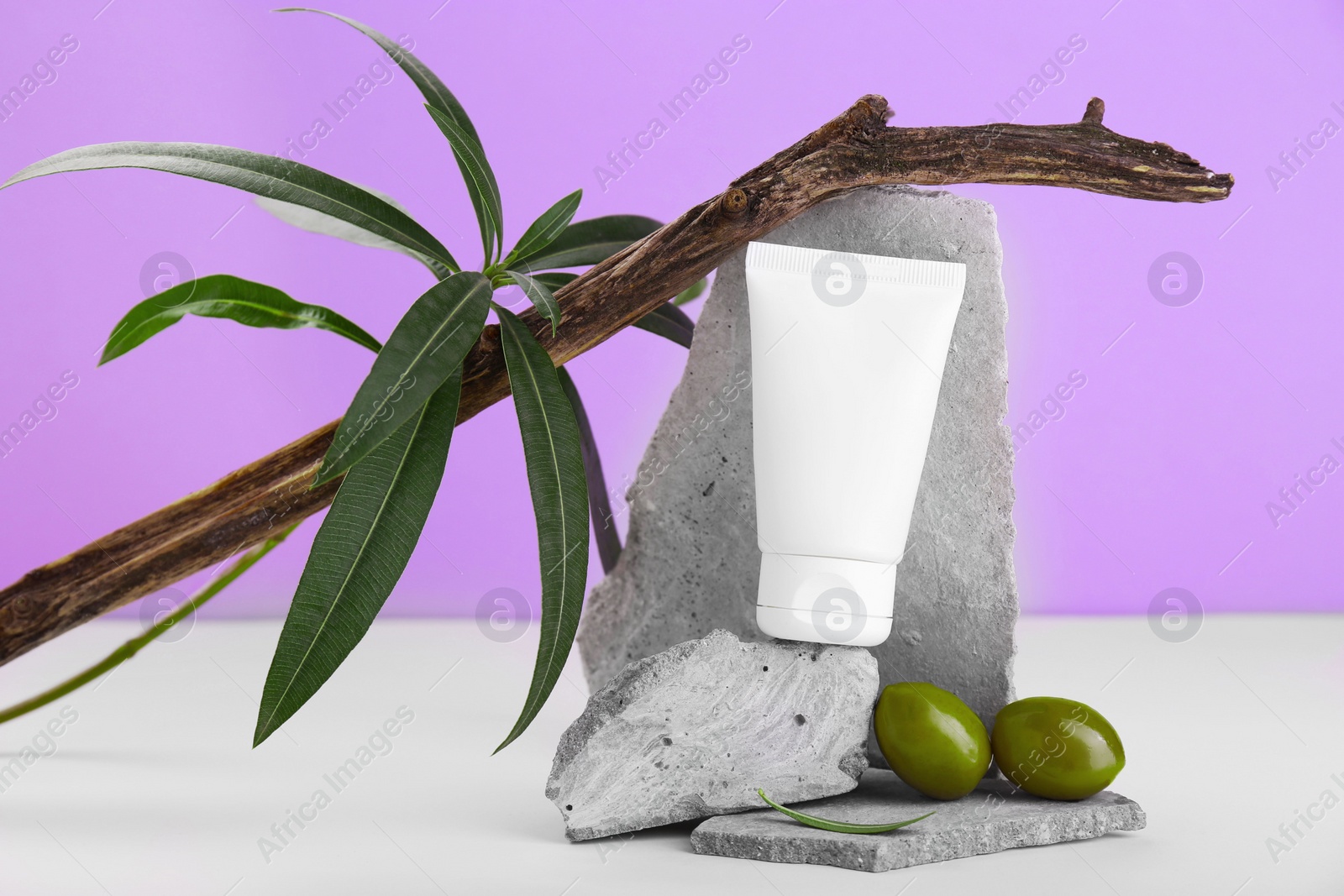 Photo of Tube of natural cream and olives on stones against purple background