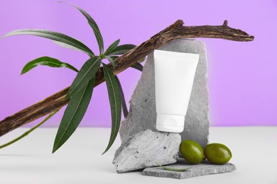Photo of Tube of natural cream and olives on stones against purple background