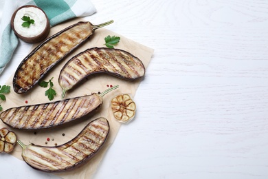 Photo of Delicious grilled eggplant halves and sauce on white wooden table, flat lay. Space for text