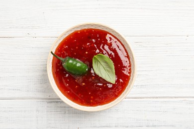 Spicy chili sauce with basil on white wooden table, top view