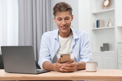 Photo of Happy young man having video chat via smartphone at wooden table indoors
