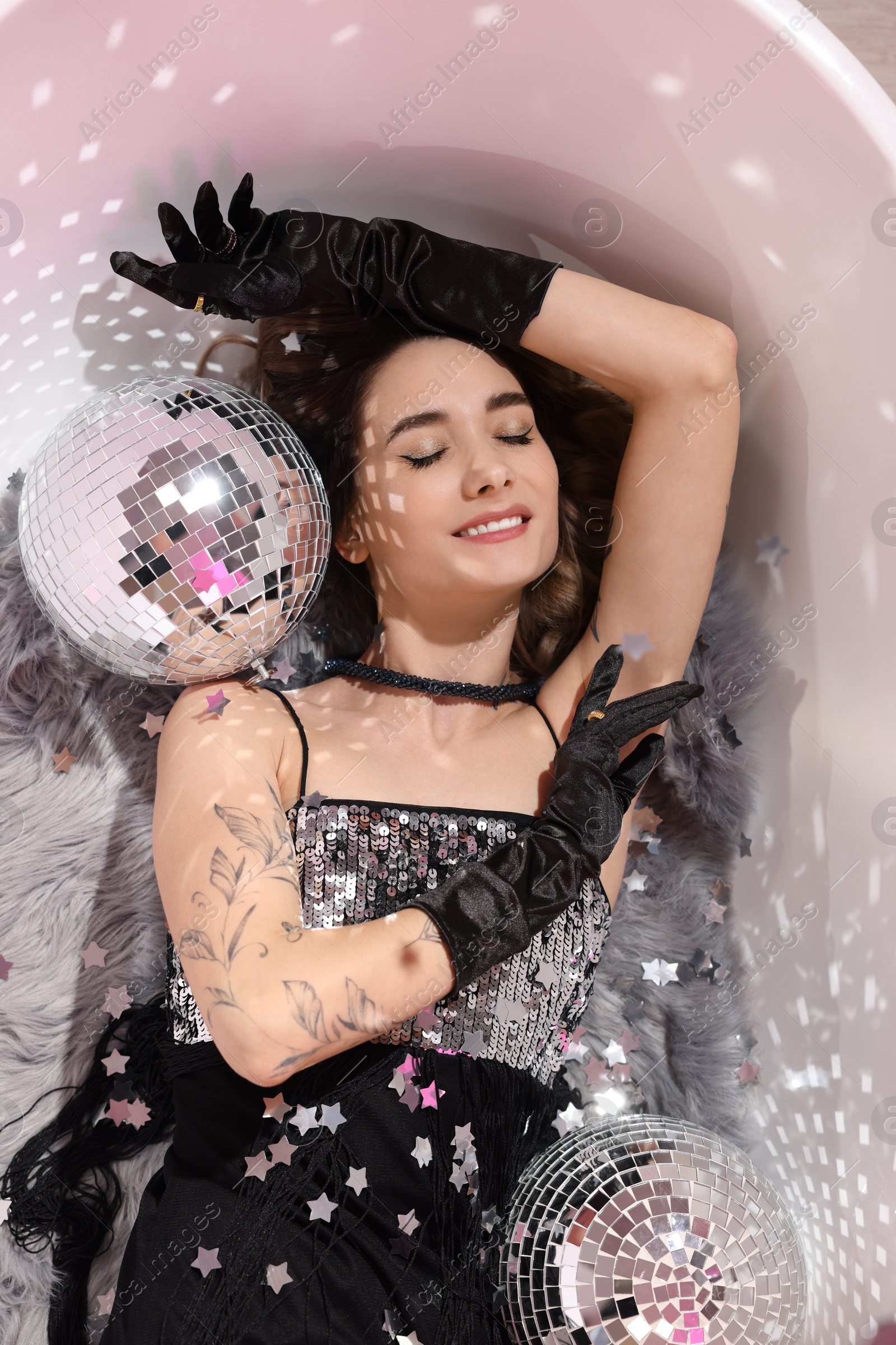 Photo of Beautiful woman in gorgeous dress among disco balls in bathtub, above view
