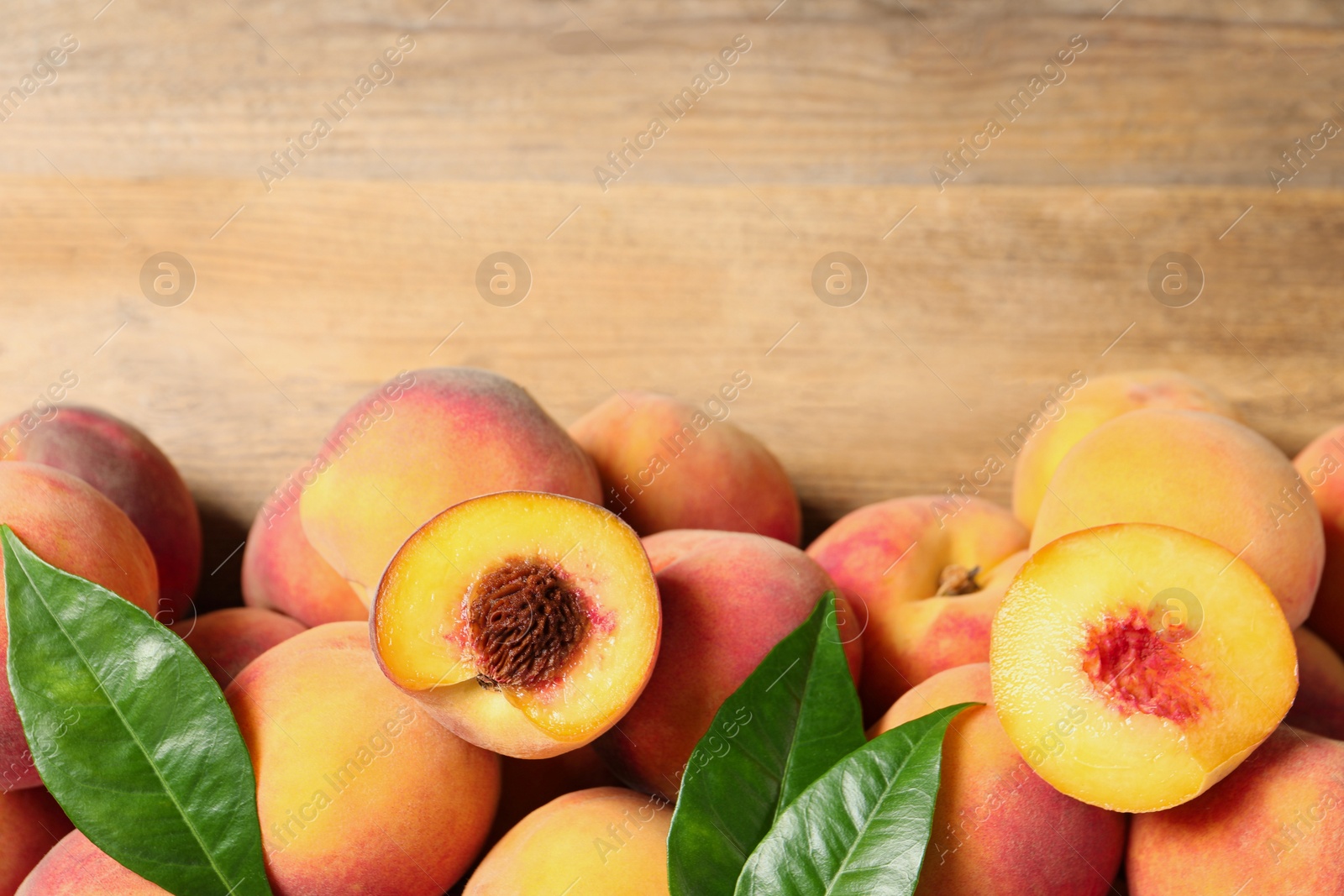 Photo of Cut and whole fresh ripe peaches with green leaves on wooden table, flat lay. Space for text