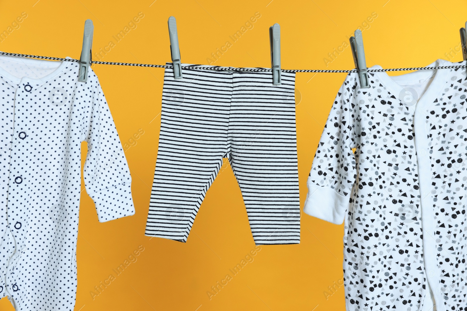 Photo of Different baby clothes drying on laundry line against orange background, closeup