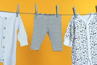 Photo of Different baby clothes drying on laundry line against orange background, closeup
