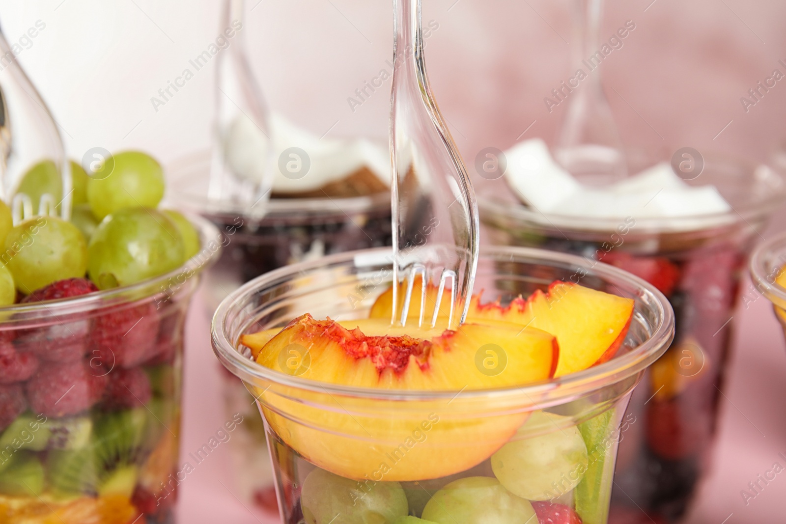 Photo of Fresh tasty fruit salad in plastic cups on pink background, closeup