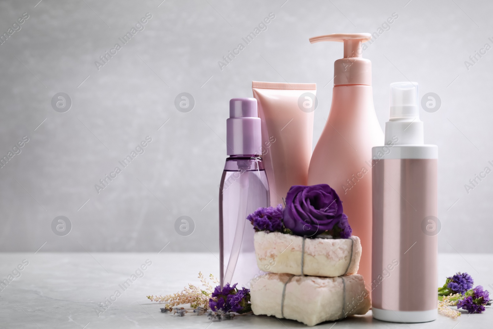 Photo of Set of hair cosmetic products and flowers on grey table. Space for text