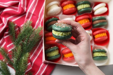 Photo of Woman with decorated Christmas macaron at table, closeup