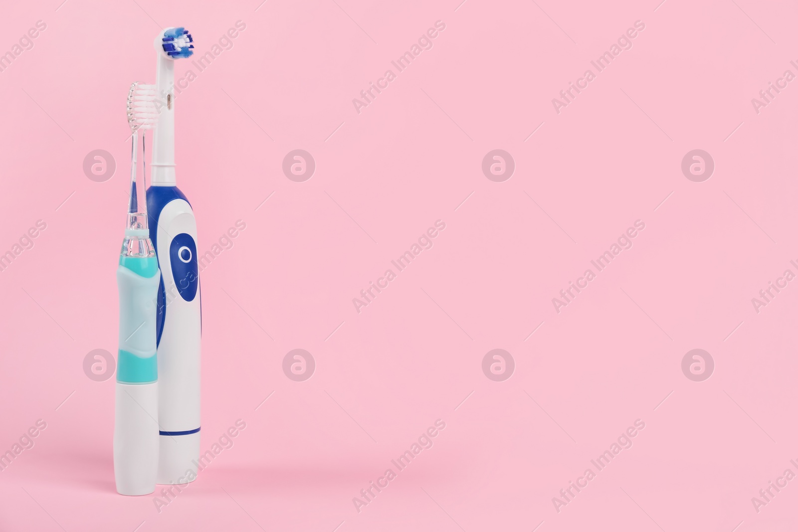 Photo of Electric toothbrushes on pink background, space for text