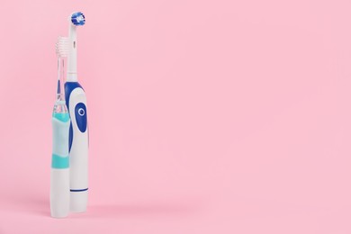 Electric toothbrushes on pink background, space for text
