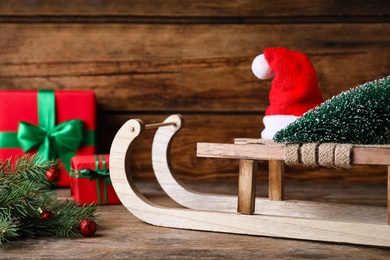 Sleigh with decorative Christmas tree and Santa hat on wooden table