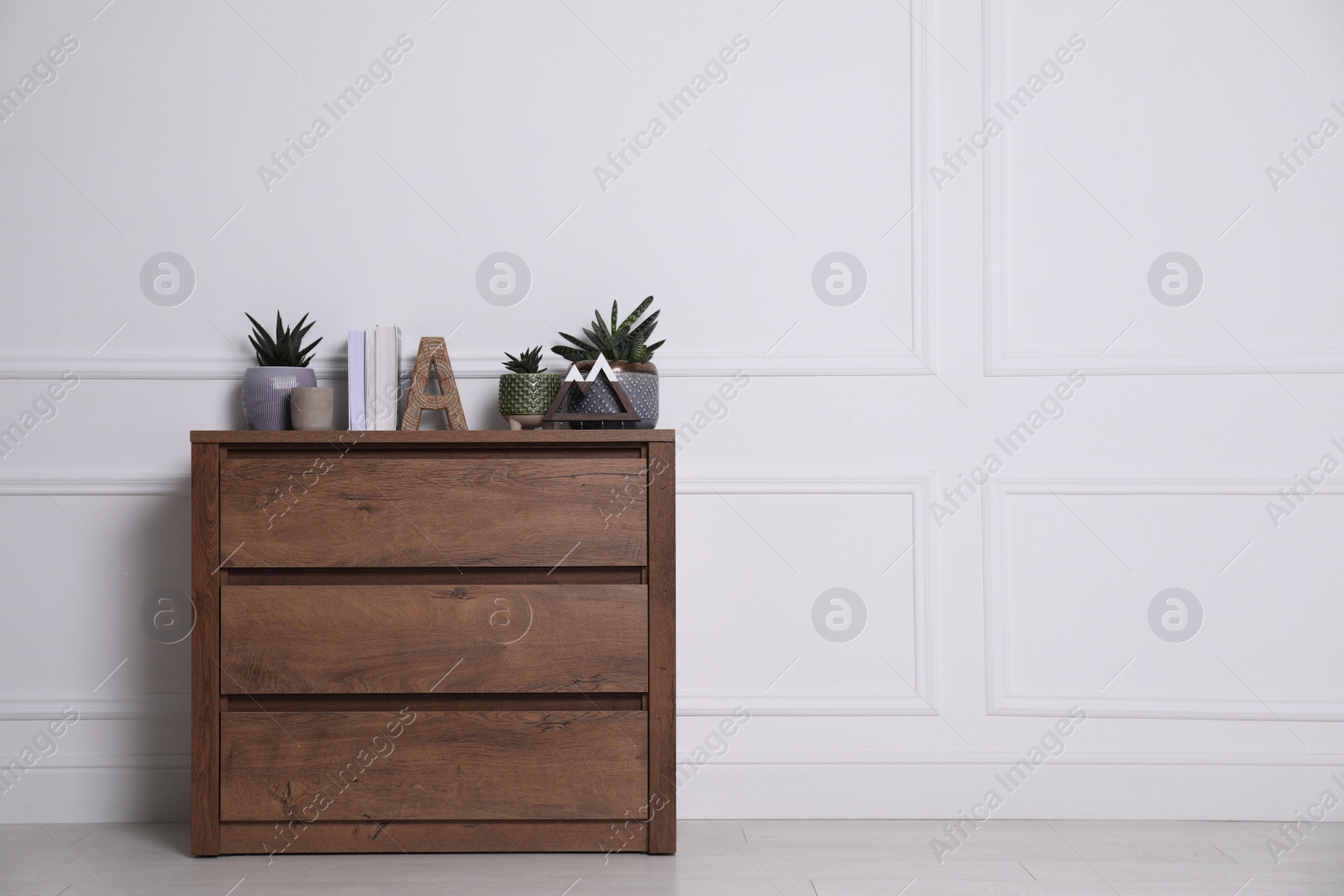 Photo of Books and beautiful plants on wooden chest of drawers near white wall indoors