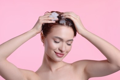 Happy young woman washing her hair with shampoo on pink background