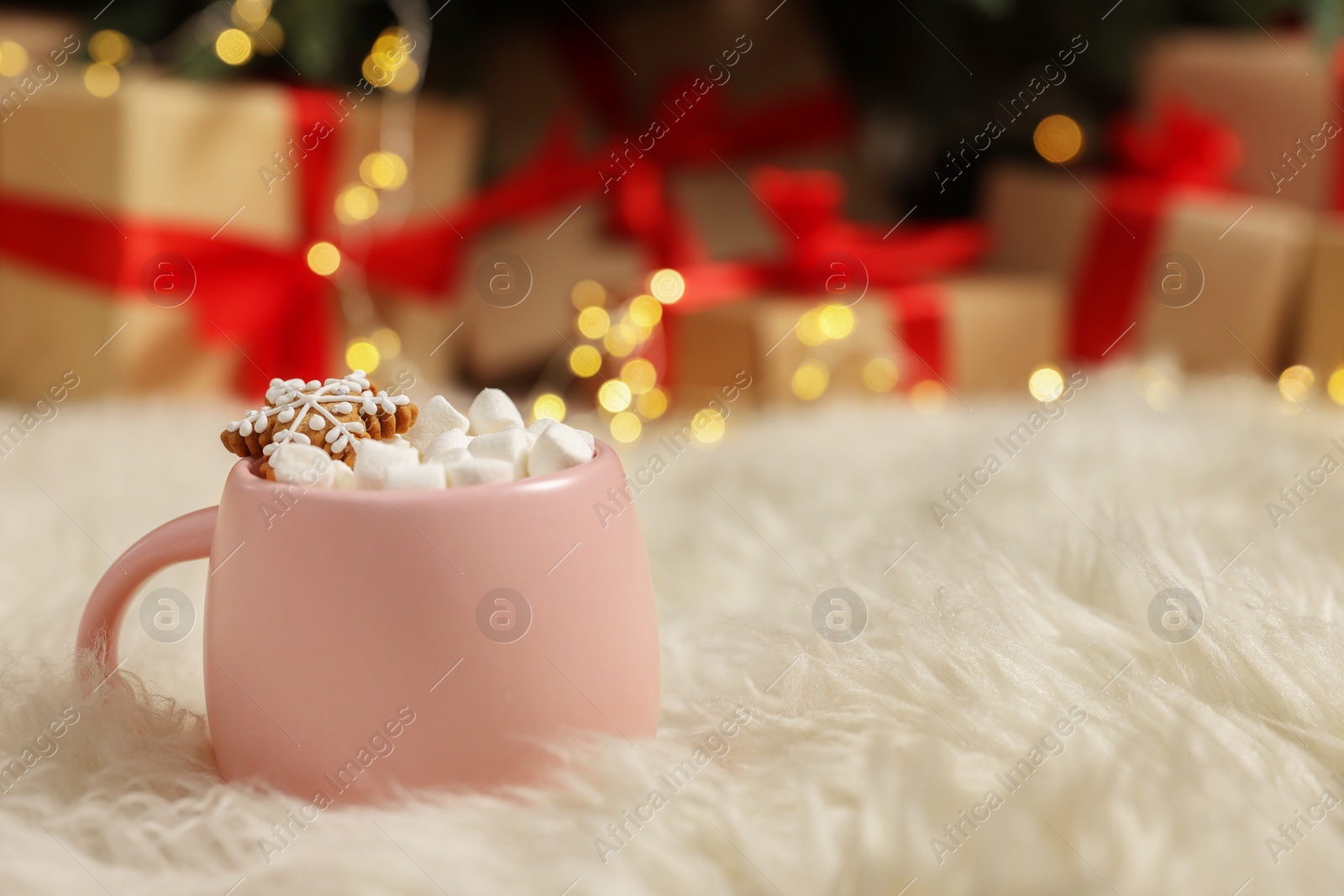 Photo of Christmas cocoa with marshmallows and gingerbread cookie in pink cup on soft carpet indoors, closeup. Space for text