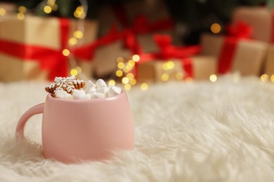 Photo of Christmas cocoa with marshmallows and gingerbread cookie in pink cup on soft carpet indoors, closeup. Space for text