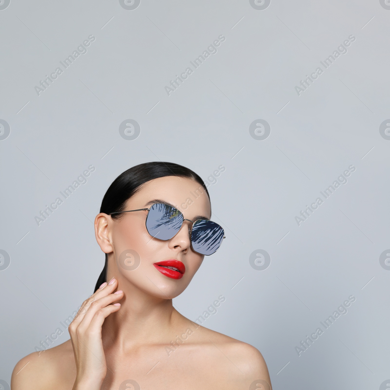 Image of Attractive woman in stylish sunglasses on light grey background, space for text. Palm leaves and sky reflecting in lenses