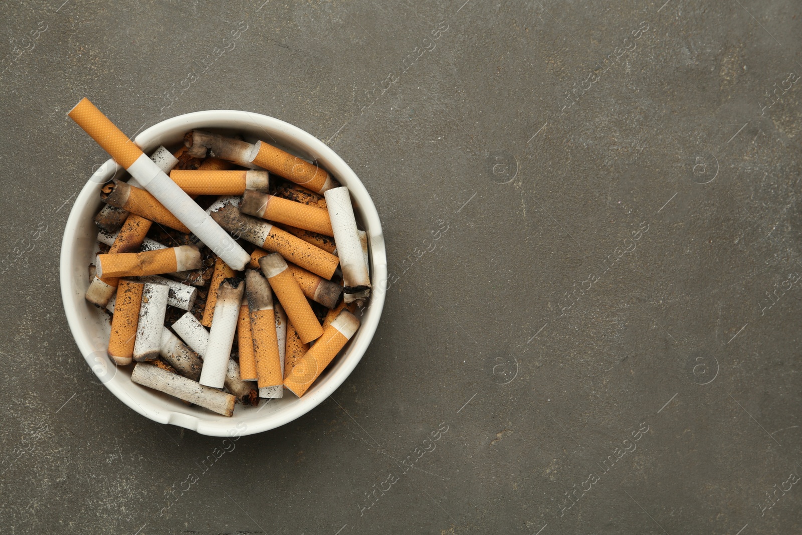 Photo of Ceramic ashtray full of cigarette stubs on grey table, top view. Space for text